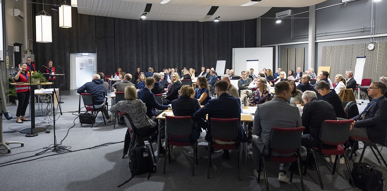Stort konferensrum med ungef&auml;r 80 personer vid bord.