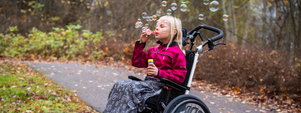 En flicka sitter i rullstol och blåser såpbubblor