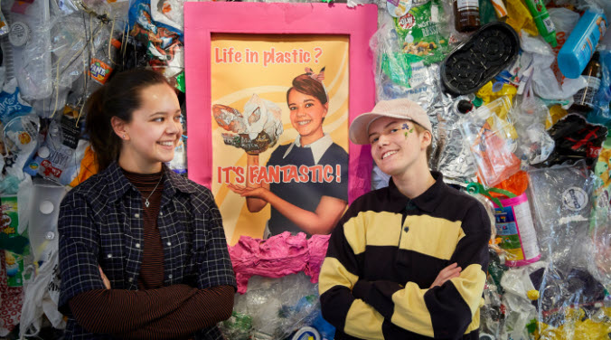 Två ungdomar står framför en vägg med plast och en tavla där det står "Life is plastic? It´s fantastic!"