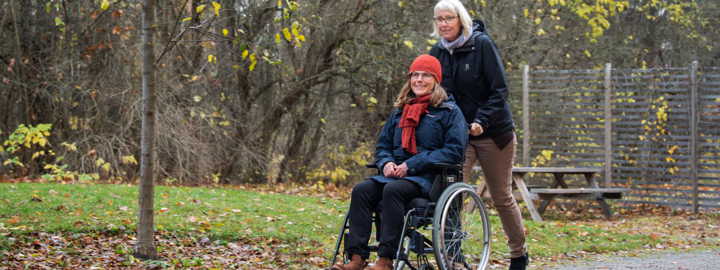 En kvinna kör en annan kvinna i rullstol
