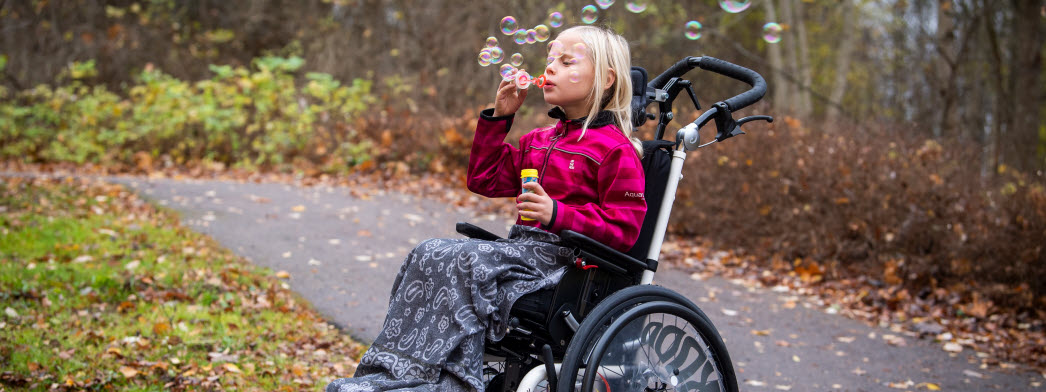 En flicka sitter i rullstol och blåser såpbubblor