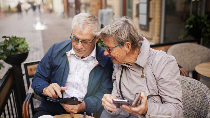 Seniorpar på café fikar och kollar i sina mobiltelefoner